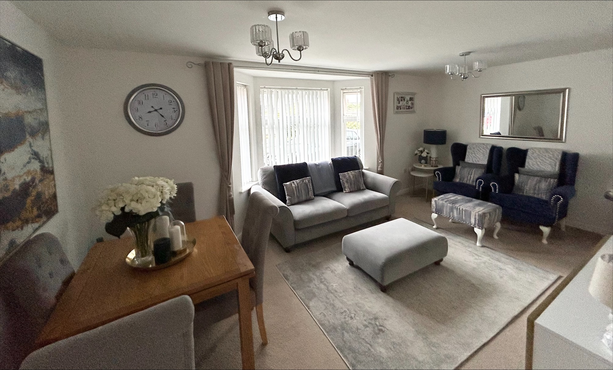 An image of a living room with grey sofa, grey footstool and brown dining table